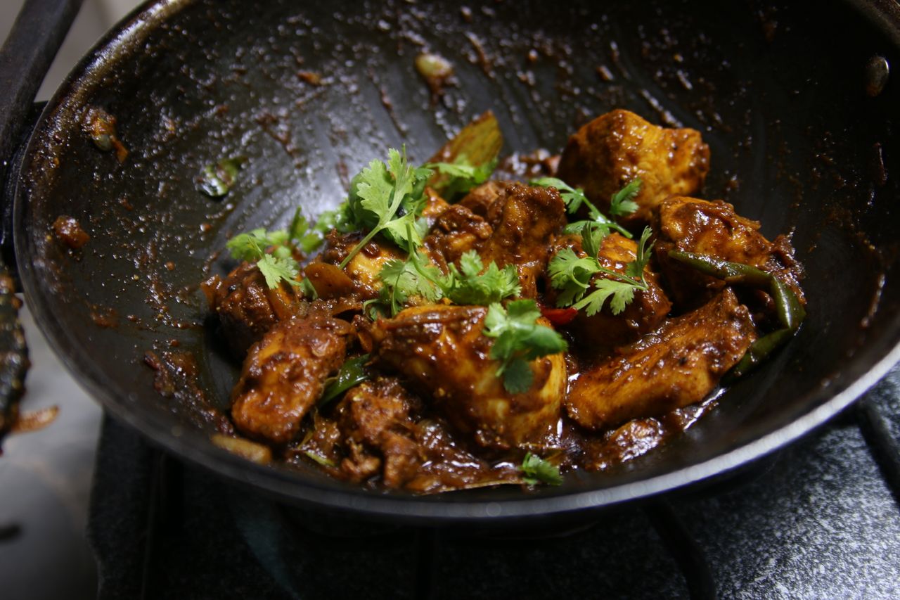 Close-up of spicy chicken curry in a wok, garnished with fresh cilantro leaves, ready to serve.