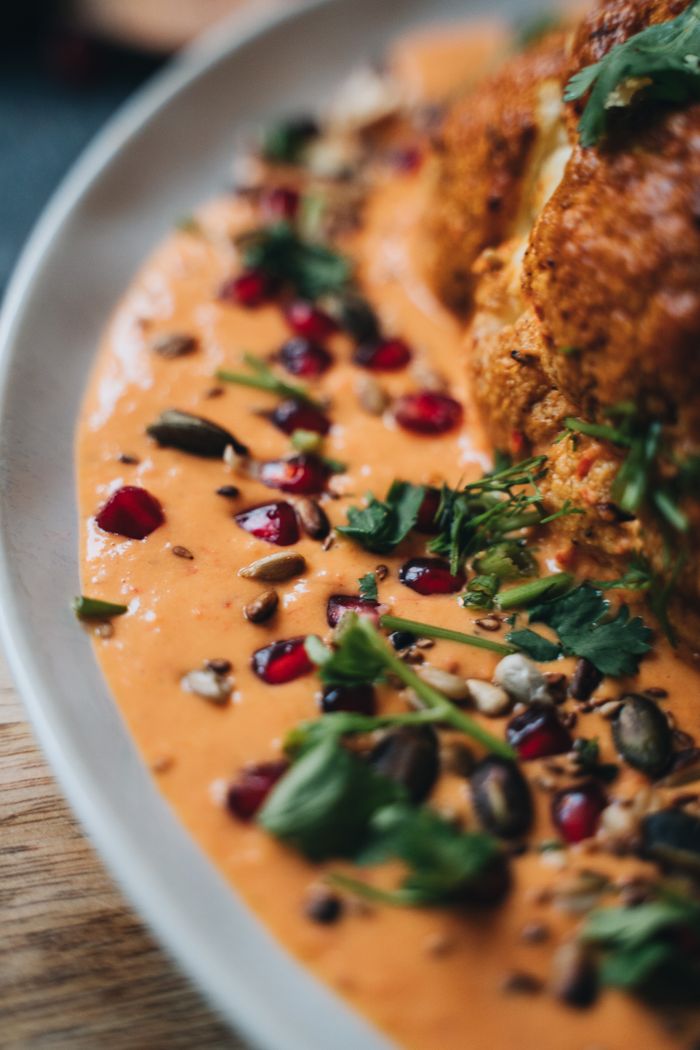 Services Close-up of roasted cauliflower served with a vibrant spiced sauce, garnished with seeds and herbs.