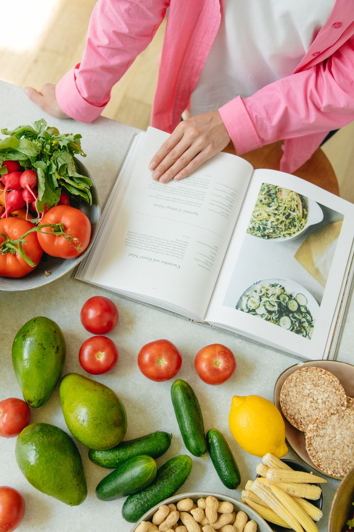 Services Overhead view of fresh vegetables and an open cookbook on a kitchen counter.